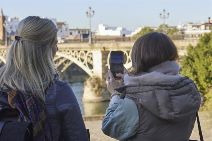 Archivo - Dos turistas fotografían el puente de Triana durante el primer día de frío, a 23 de noviembre de 2021 en Puente de Triana en Sevilla (Andalucía, España). Imagen de archivo.