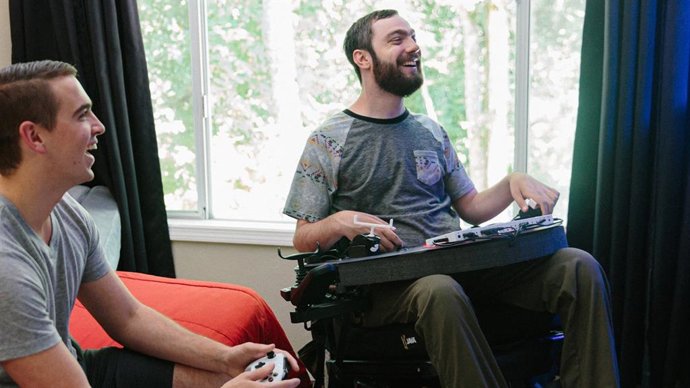 Duas pessoas jogando Xbox, uma delas com controles adaptados.