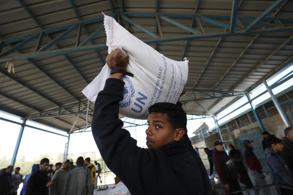 Trabajadores trasladan sacos de harina mientras los palestinos hacen cola para recibir ayuda alimentaria de UNRWA