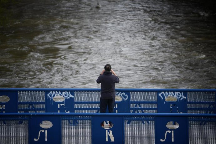 Una persona fotografía la crecida del río, en el parque lineal del Manzanares, a 20 de marzo de 2025, en Madrid (España).