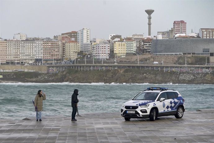 Archivo - Dos personas pasan al lado de un coche de policía local, a 4 de noviembre de 2023, en A Coruña, Galicia.