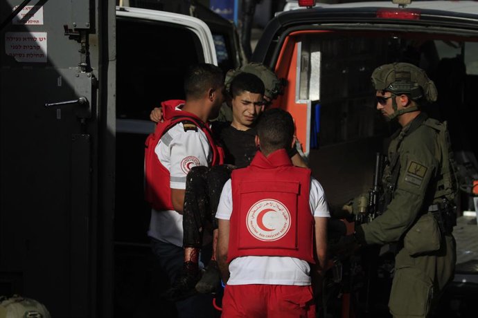 Archivo - Arquivo - 19 de setembro de 2024, Territórios Palestinos, Qabatiyah: Membros da Sociedade do Crescente Vermelho Palestino ajudam um menino ferido enquanto um soldado do exército israelense permanece de pé durante um ataque na cidade de Qabatiyah