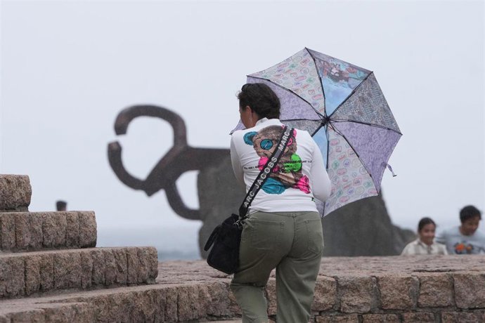 Archivo - Una mujer camina con un paraguas junto al Peine del Viento, en San Sebastián