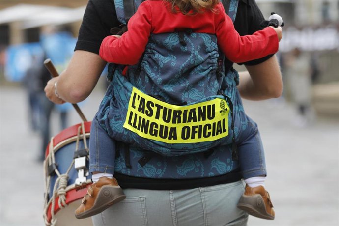 Archivo - Una mujer lleva una niña pequeña cargada a la espalda, con una pegatina donde se lee "El asturiano lengua oficial", en una manifestación por la Oficialidad del Asturiano.