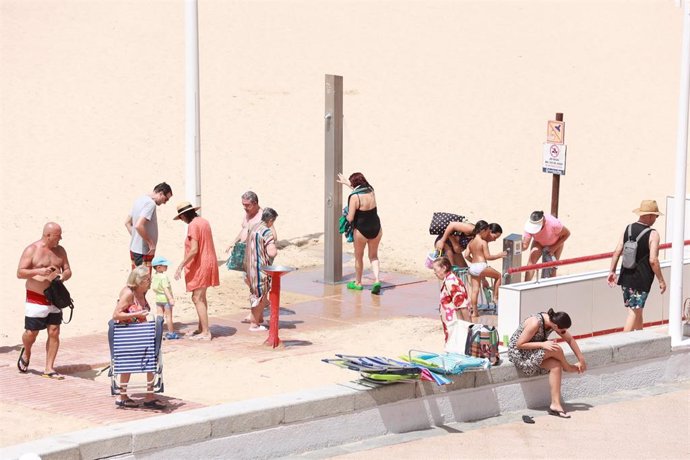 Archivo - Bañistas hacen uso de las duchas de la playa de la Victoria antes del corte previsto debido a la sequía en verano de 2023.