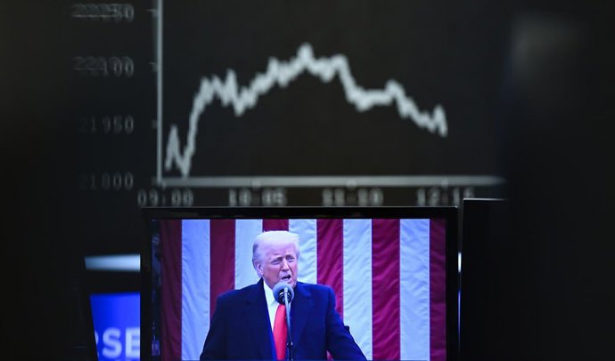 dpatop - 03 April 2025, Hesse, Frankfurt/Main: Behind a television monitor showing US President Donald Trump, the display board with the DAX curve shows falling share prices. The tariff package announced by US President Trump has pushed share prices sharp