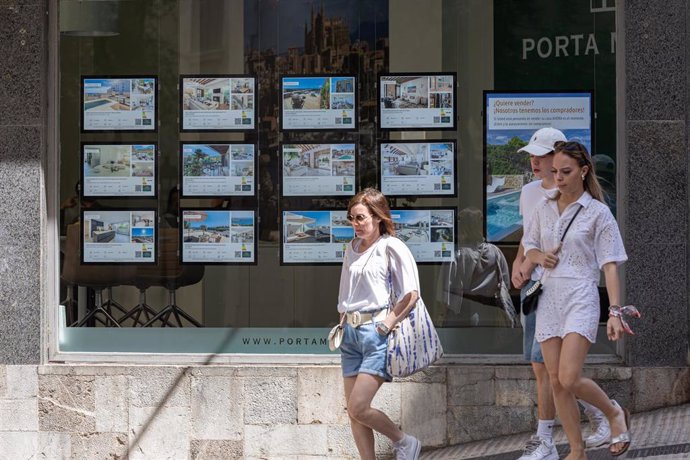 Archivo - Varias personas pasan junto a los anuncios de viviendas en venta en una inmobiliaria en Palma.