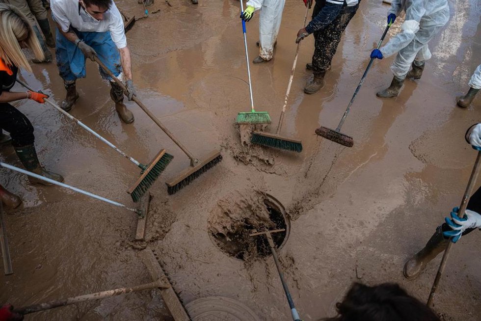 Archivo - Varias personas retiran barro con cepillos en una alcantarilla de Alfafar