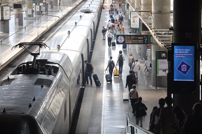 Archivo - Varios pasajeros con maletas junto a un tren en la estación Madrid-Puerta de Atocha.