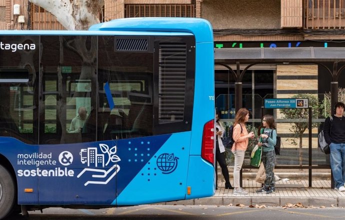 Archivo - Personas esperan en una parada junto a un autobús