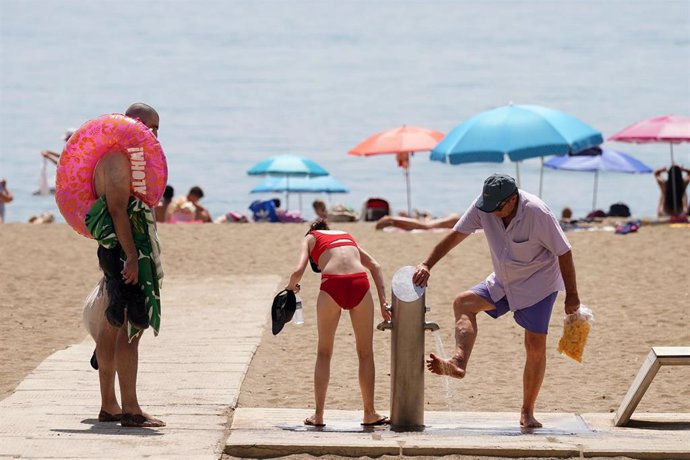 Archivo - Varias personas se duchan en los lavapies de la playa en La Malagueta en una imagen de archivo 