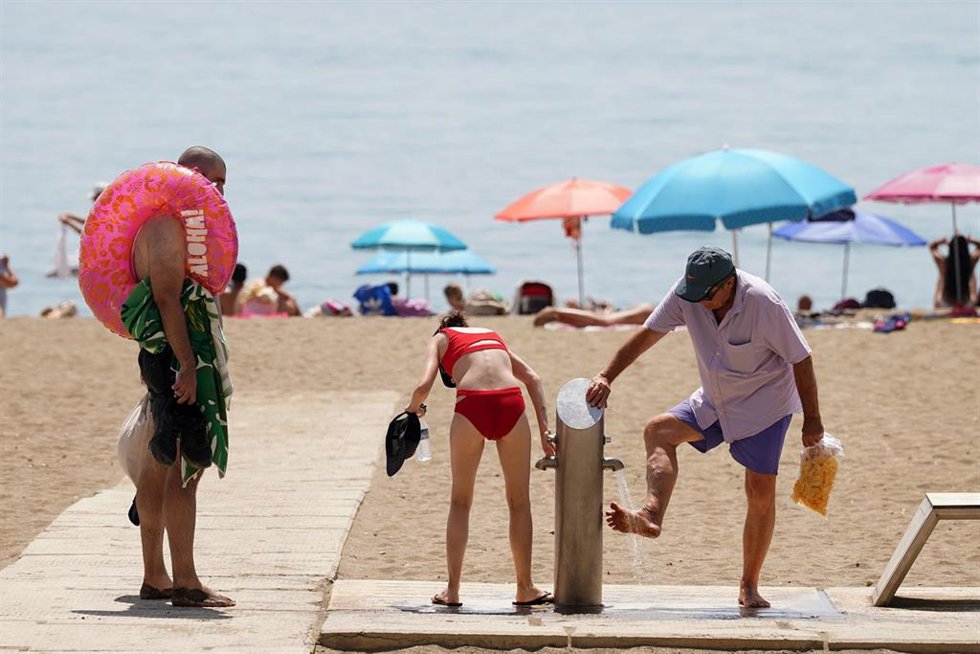 Archivo - Varias personas se duchan en los lavapies de la playa en La Malagueta en una imagen de archivo 