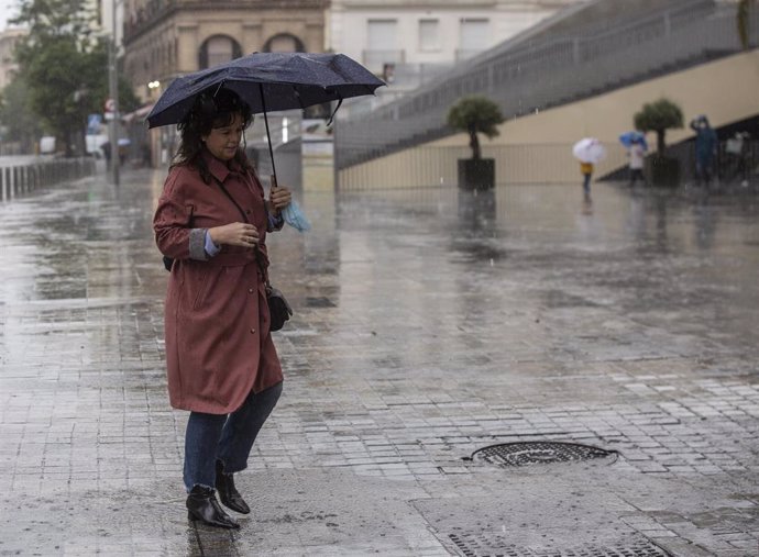 Archivo - Una mujer se resguarda de la lluvia bajo su paraguas durante la alerta amarilla por tormentas en Sevilla, (Andalucía, España), a 14 de mayo de 2020.