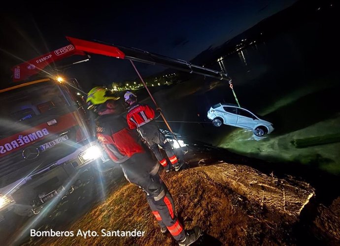 Los Bomberos alzan a un coche caído al agua en la zona de la playa de Los Peligros.