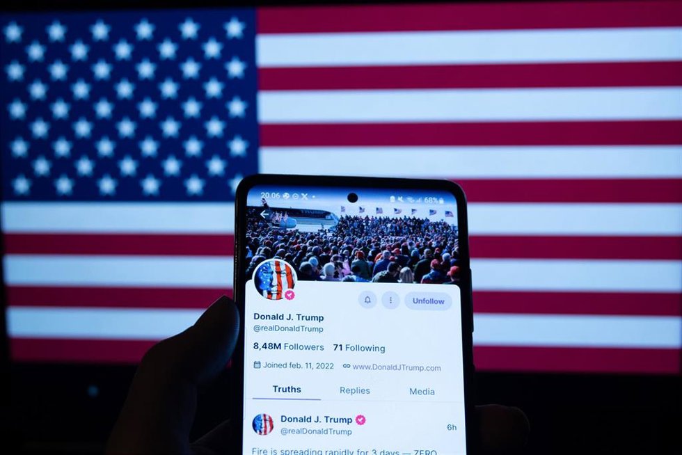 Archivo - Imagen de un móvil con la página de Donald Trump en Truth Social ante una bandera de Estados Unidos