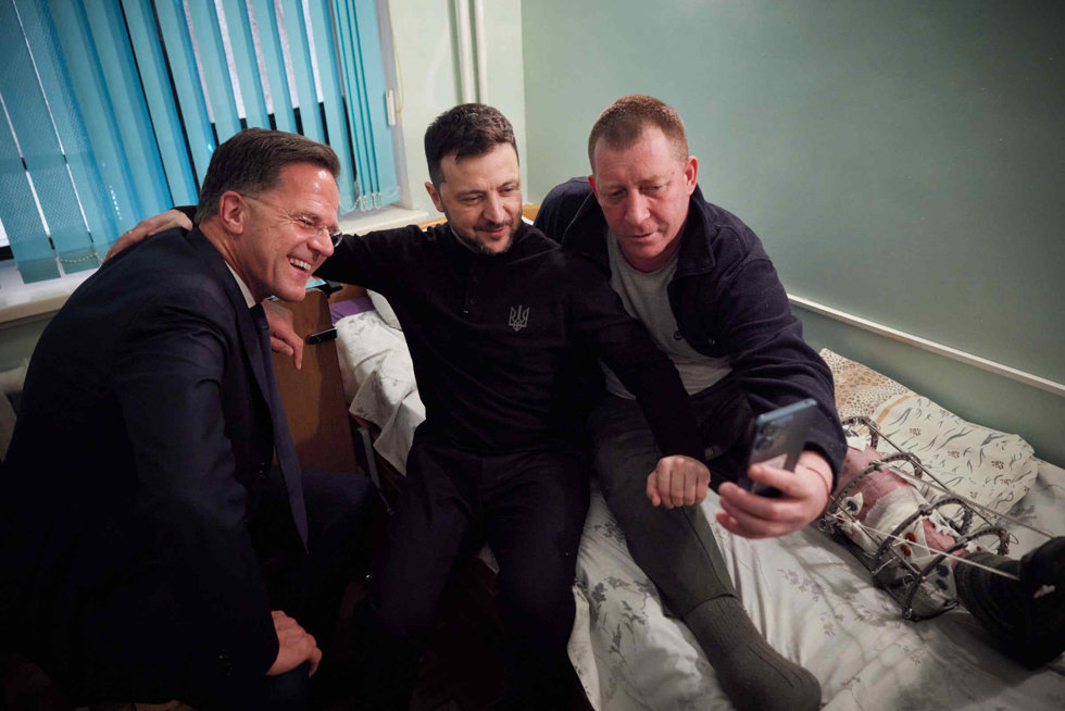 El presidente de Ucrania, Volodymir Zelenski (c) y el secretario general de la OTAN, Mark Rutte, posan para un selfi con un hombre herido durante una visita a un hospital de Odesa. 