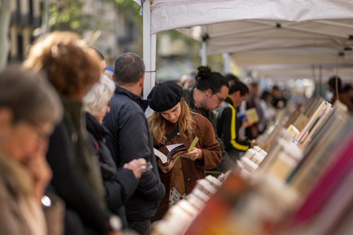 Archivo - Varias personas miran libros en un puesto durante el día de Sant Jordi 2024, a 23 de abril de 2024, en Barcelona
