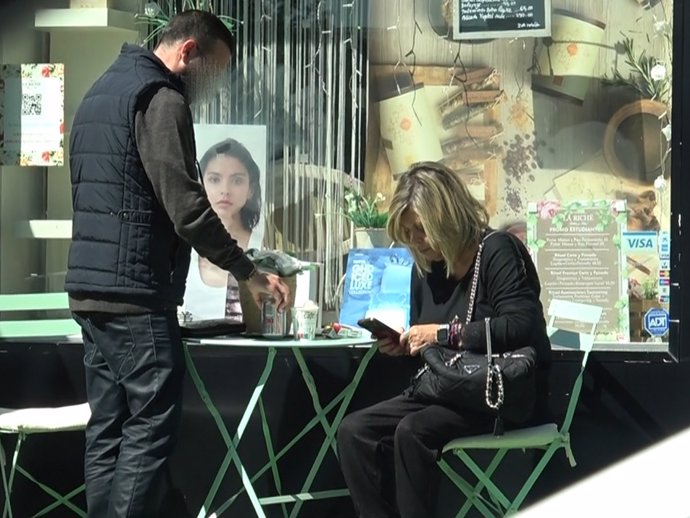 Terelu Campos mirando su móvil mientras su chófer le sirve la Coca-Cola