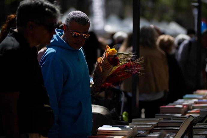 Transeúnte paseando con rosas en los puestos de libros, durante la Diada de Sant Jordi 2025, a 23 de abril de 2025, en Barcelona, Cataluña (España). Barcelona vuelve a vivir una nueva Diada de Sant Jordi, en la que se llena de libros y rosas, en una edici
