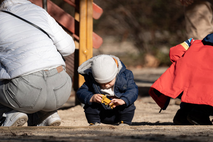 Varios niños juegan con sus juguetes y sus padres en un parque.