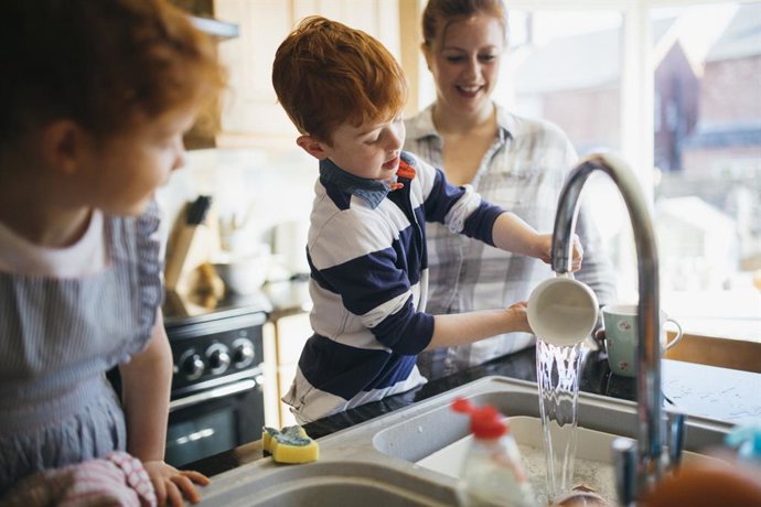Archivo - Niños fregando los platos con su madre en le cocina.