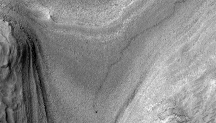 El rover Curiosity de la NASA aparece como una mancha oscura en esta vista de contraste mejorado capturada el 28 de febrero de 2025 por la cámara HiRISE a bordo del Mars Reconnaissance Orbiter de la NASA.