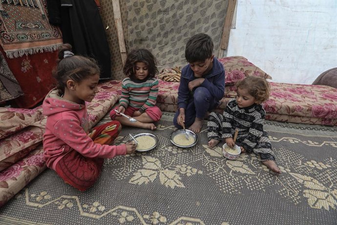 Archivo - Niños palestinos comen alimentos entregados por una organización caritativa en Deir al Balá en medio de la ofensiva militar de Israel contra la Franja de Gaza (archivo)