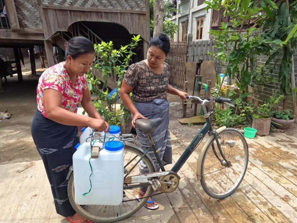 Dos mujeres birmanas transportan agua en garrafas.