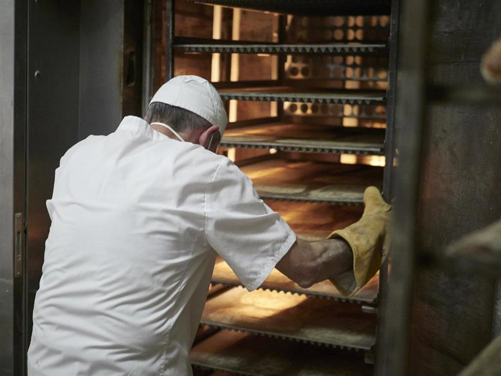 Archivo - Un trabajador protegido con mascarilla y guantes maneja bandejas para cocer el pan en el obrador panadería 'Panadero de Eugui' durante en el día 32 del estado de alarma, uno de los establecimientos que puede permanecer abierto por despachar al