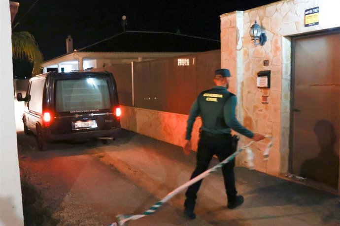 Un coche fúnebre y un agente de la Guardia Civil junto a la puerta donde tuvo lugar el suceso