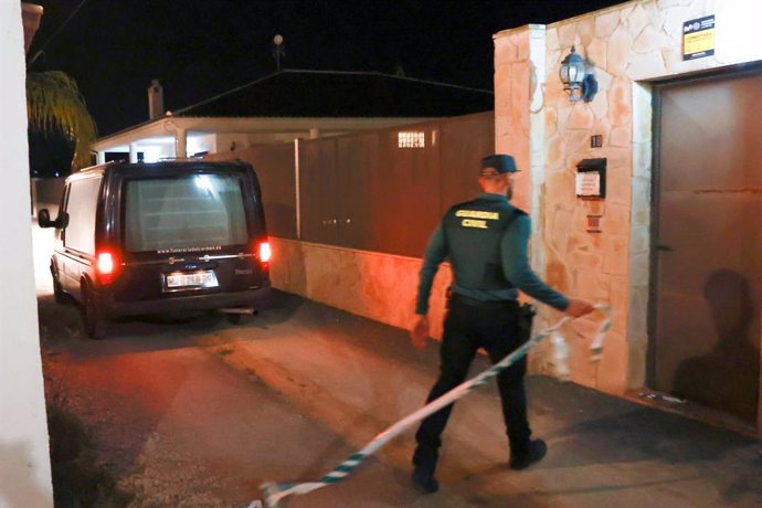 Un coche fúnebre y un agente de la Guardia Civil junto a la puerta donde tuvo lugar el suceso