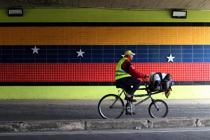 Un hombre pasa en bicicleta ante un mural con la bandera de Venezuela en la ciudad de Valencia