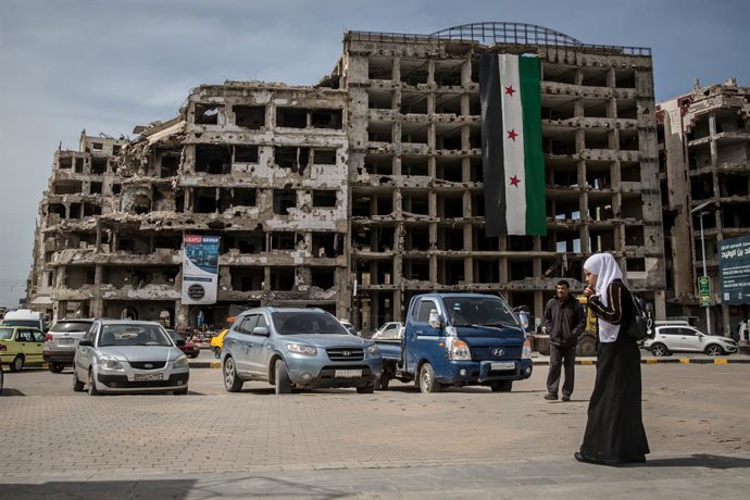 Archivo - Arquivo - 26 de março de 2025, Homs, Síria: Uma mulher é vista em frente a uma bandeira revolucionária enrolada no centro de Homs. Homs, a terceira maior cidade da Síria, já foi conhecida como a "capital" da revolução.