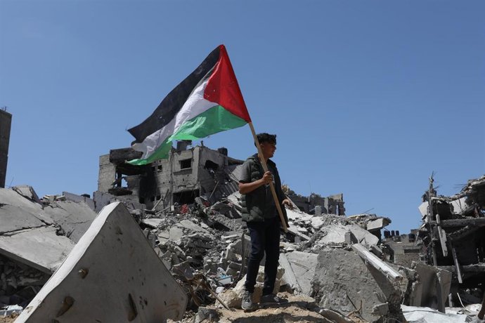 Archivo - Un joven sujeta una bandera palestina sobre los restos de edificios bombardeados por Isarel en la Franja de Gaza