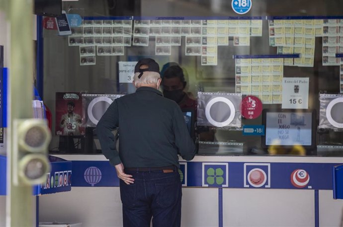 Archivo - Dos personas compran lotería en una Administración 
