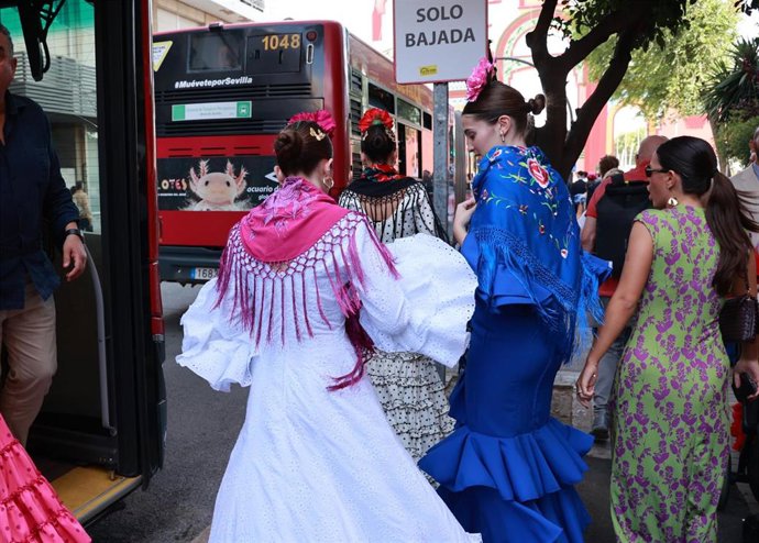 Varias mujeres de flamenca bajan de uno de los autobuses con parada en la Feria.