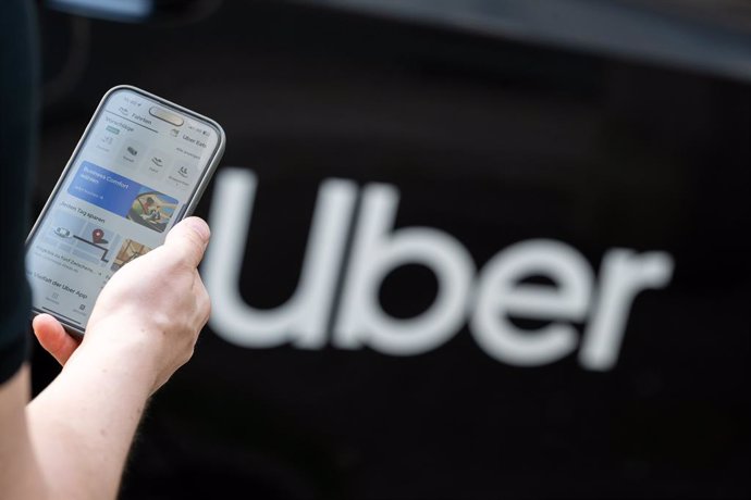 Archivo - FILED - 08 August 2024, Berlin: A man stands in front of a rental car with a sign from the mobility service provider and ride broker Uber and holds his smartphone with the company's app in his hand. Photo: Sebastian Gollnow/dpa