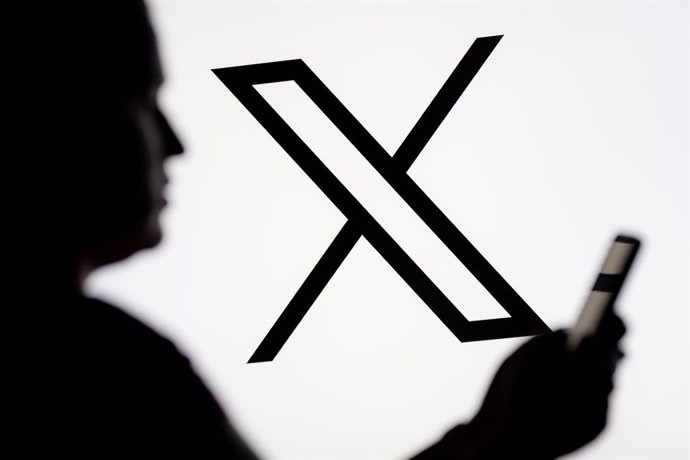 Archivo - March 7, 2025, Poland: In this photo illustration, a woman seen looking at a smartphone with the X (Twitter) logo displayed in the background.