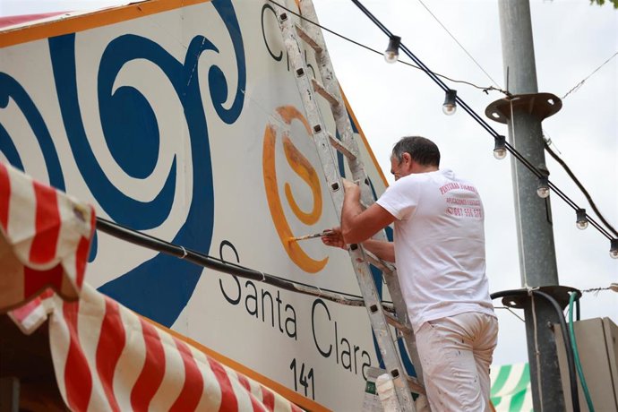 Un trabajador lleva a cabo labores de pintura en la pañoleta de una caseta de la Feria.
