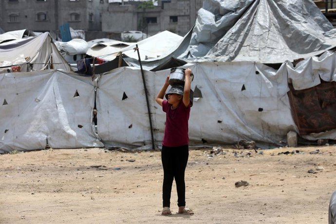 12 May 2025, Palestinian Territories, Gaza: A Palestinian child holds a food pot to receive food distributed by charitable organizations, in Gaza city. Food crisis in the Gaza Strip deepens day by day due to the closure of border crossings, as they face f