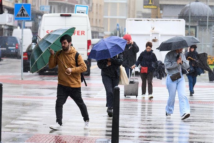 Archivo - Varias personas se cubren de la lluvia y el viento con paraguas.- Archivo