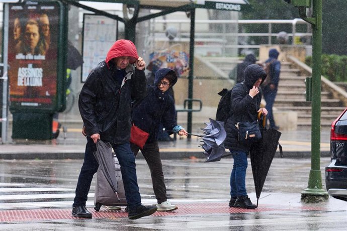 Archivo - Varias personas tratan de cubrirse de la lluvia y el viento en Santander