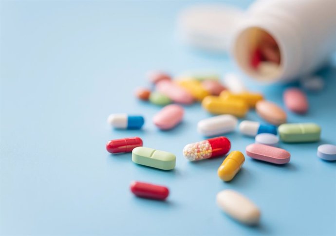 Archivo - Píldoras multicolores dispersas del recipiente de plástico blanco para medicamento