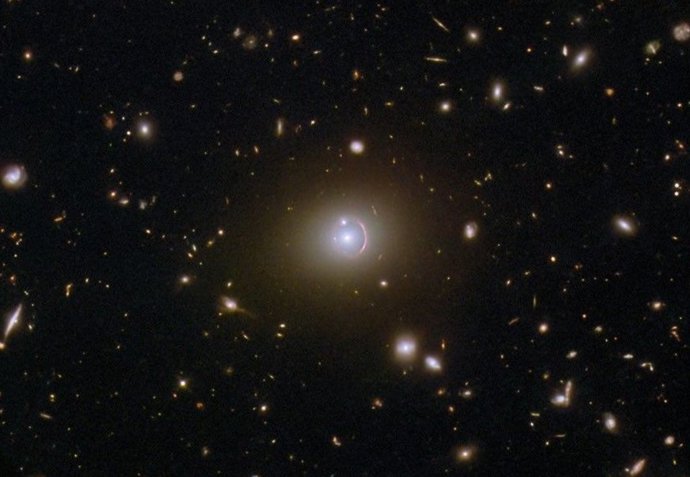 Esta imagen del telescopio espacial Hubble de la NASA/ESA muestra la galaxia remota HerS 020941.1+001557, que aparece como un arco rojo que rodea parcialmente una galaxia elíptica en primer plano.