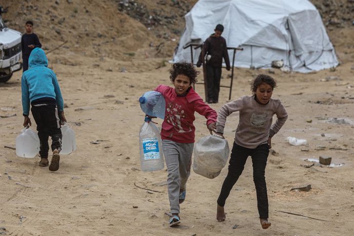 Archivo - 21 March 2025, Palestinian Territories, Gaza: Displaced Palestinian children run around holding jerry cans in front of makeshift tents set up at Between the destroyed buildings of the Islamic University in Gaza City. Photo: Omar Ashtawy/APA Imag