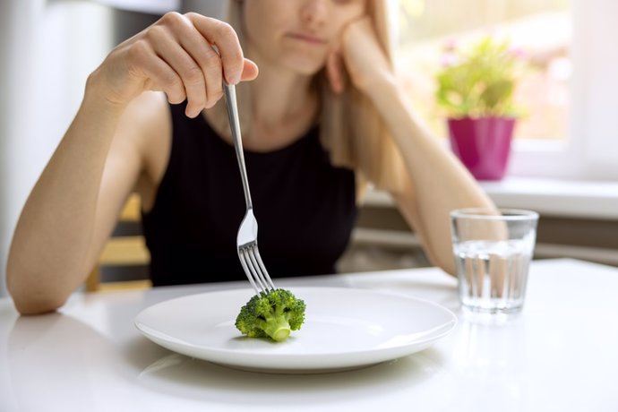 Archivo - Problemas de dieta, trastorno alimentario: mujer infeliz que mira una pequeña porción de brócoli en el plato.