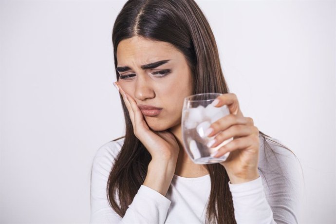 Archivo - Mujer joven con dientes sensibles y vaso de agua fría con hielo.
