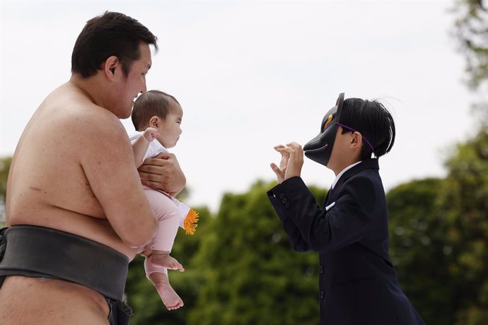 April 26, 2025, Tokyo, Japan: A man wearing a devil mask makes a baby cry for good luck at the annual Crying Baby Sumo event held near Sensoji Temple. Families and visitors gather in front of the bronze statue of kabuki actor Ichikawa Danjuro IX where sum