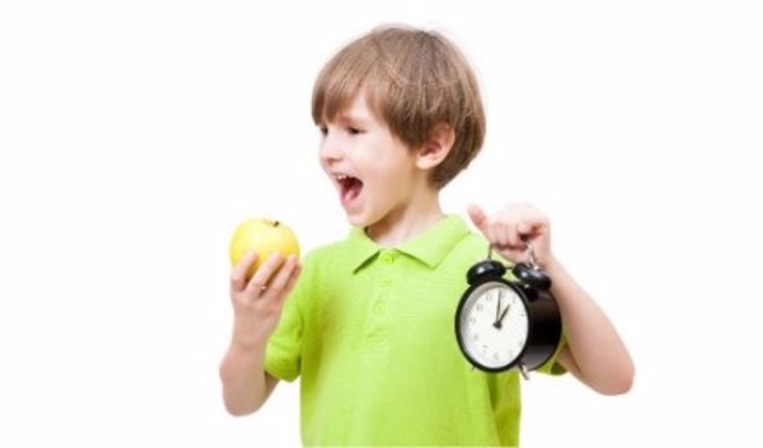 Un niño sujeta una manzana y un reloj.