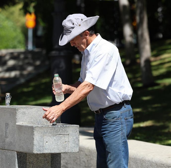 Archivo - Un hombre llena una botella de agua de una fuente.
